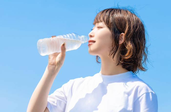 青空の下でペットボトルの水を飲む女性の写真