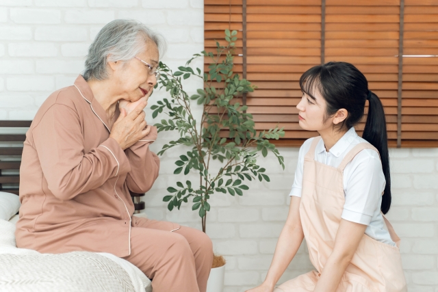 痛がる高齢者女性とエプロン姿の女性(虫歯)